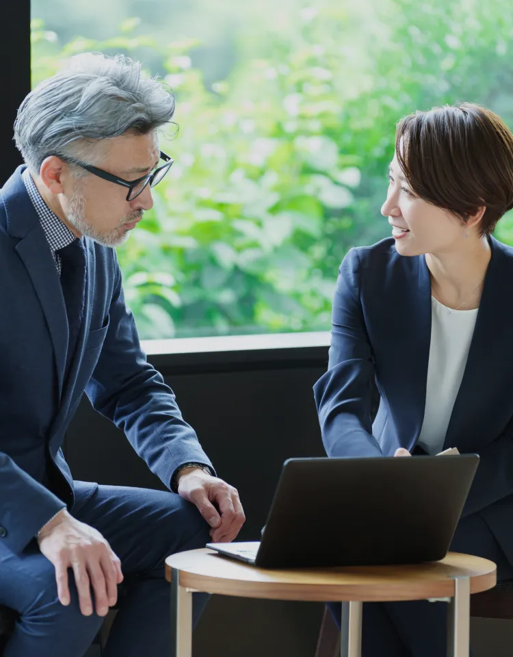 オフィスでノートパソコンを使いながら話し合う二人のビジネスパーソンの様子