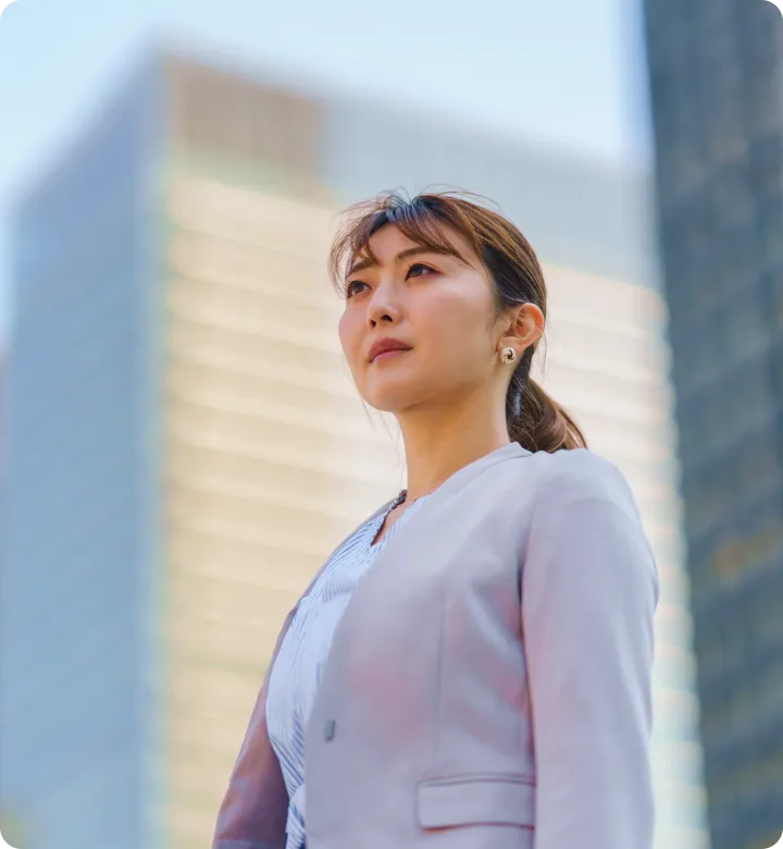 ビジネススーツを着た女性が高層ビルの前に立っている様子