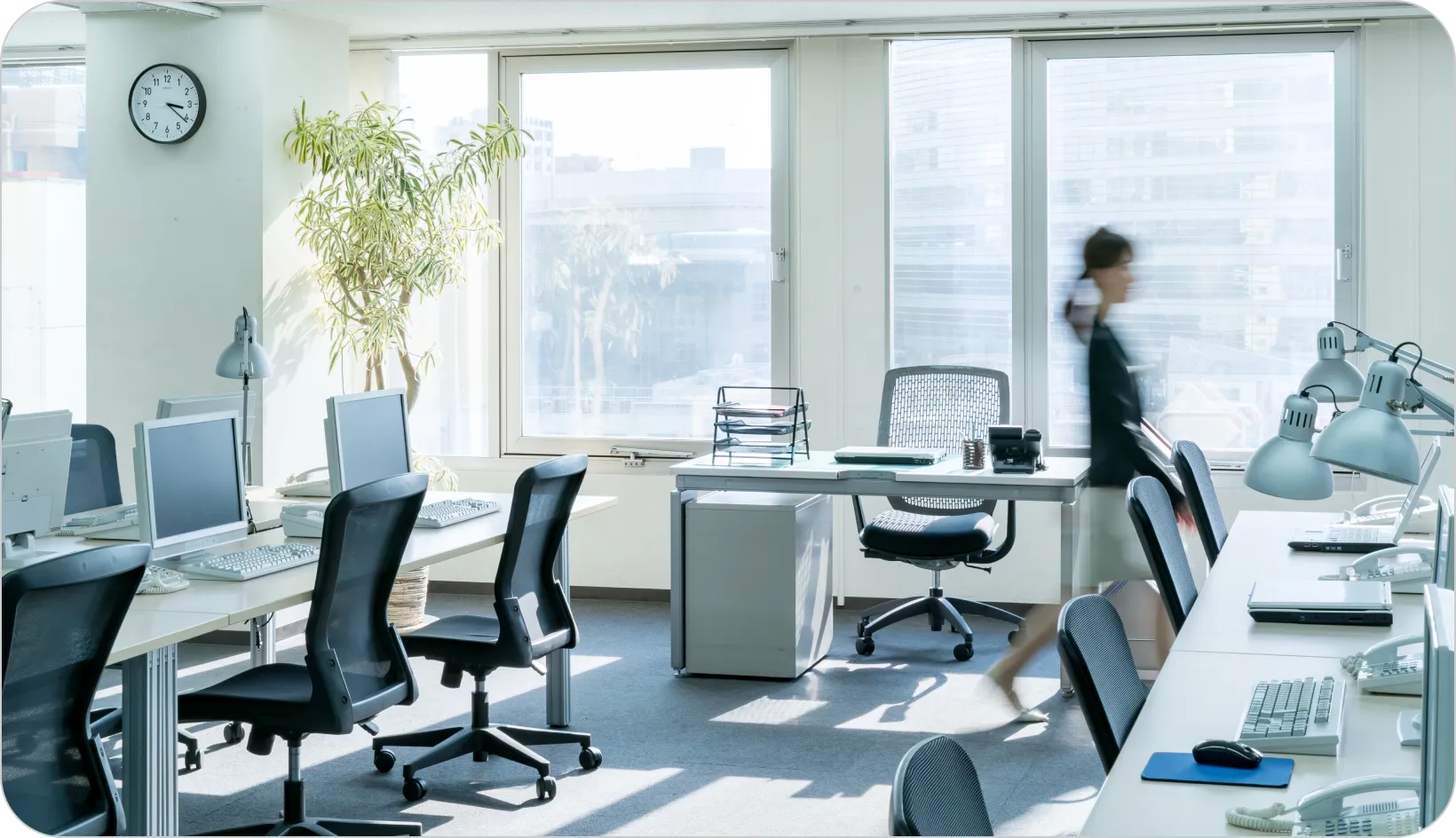 オフィス内を歩く女性の姿が描かれた画像。周囲にはデスクや椅子が配置されている。